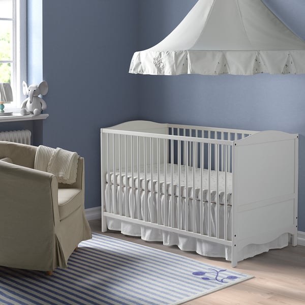 White SMÅGÖRA crib, grey chair, striped rug, elephant figurine.