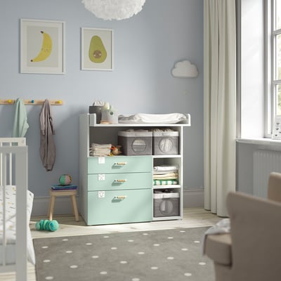 Baby room with blue SMÅSTAD changing table & dresser near window. Room crib, light blue walls, cloud pendant light, & baby supplies.