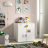 Childs room with SMÅSTAD storage, toys, and wall art. Cabinet holds various items with clock and stuffed animals on top.