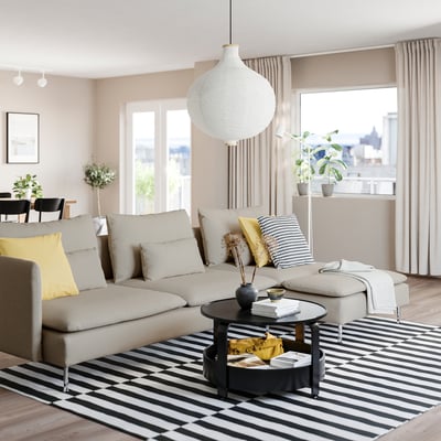 Modern living room with SÖDERHAMN beige sofa, bold rug, pendant light, and city view. Neutral tones with black & yellow accents.