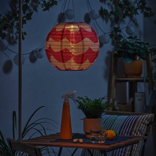 Cosy outdoor seating with a solar-powered lantern, a table, and plants. The lantern glows warmly, illuminating the space at dusk.