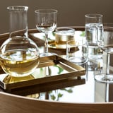 Clear glass carafe and glasses on brass tray. Carafe for decanting wine or serving water, showcasing contents.