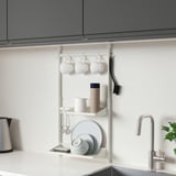 Modern white SUNNERSTA kitchen rack holding cups, plates, and mugs under grey cabinet.