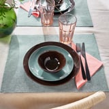 Modern table setting with turquoise plates, glasses, and cutlery on green place mats.