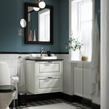 Modern blue bathroom with TÄNNFORSEN white vanity, black and white floor tiles, and greenery. Vanity fits neatly under large mirror.