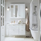 Modern white bathroom with TÄNNFORSEN vanity and cabinet. Sink, mirror, and bathtub. Gold accents and minimalist decor.