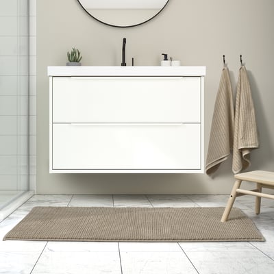 Modern bathroom with floating vanity, black fixtures, round mirror, and beige bath mat on grey tiles.