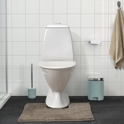 Modern bathroom: white toilet, light beige mat, blue brush, hanging towel, dark floor.