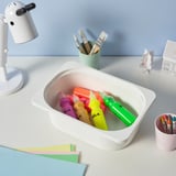 White desk with colourful art supplies in white container labelled TROFAST, lamp, brushes, and paper.