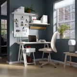 Modern home office: white TROTTEN desk, flintan chair, green wall, shelves with plants.