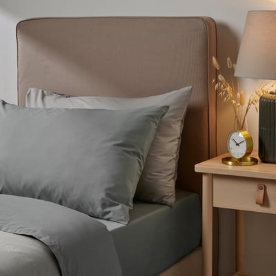 Bed with grey pillowcases, padded headboard, bedside clock & dried flowers.