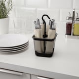 Black mesh cutlery holder with handle sits on counter, holding silverware with plates, glasses, and oil dispensers nearby.
