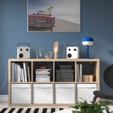 Modern living room with blue wall, vintage car poster, sleek storage, black-and-white rug, and VAPPEBY speakers.