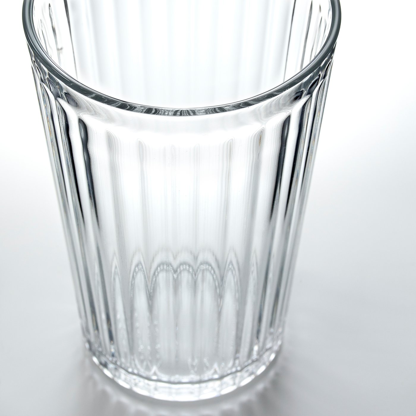 Clear glass tumbler with vertical ridges, resting on a reflective surface, showcasing its sleek and durable design.