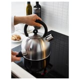 Hand lifts whistling VATTENTÄT kettle from modern hob after boiling water. Sleek design handles prominently featured.
