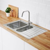 Stainless steel sink with integrated drainboard and separate compartments, set on wooden counter with modern tap and plant.