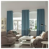 Modern living room with beige sofas, white coffee table, and blue curtains on large windows.