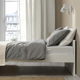 Minimalist bed with grey linens, slatted design for easy cleaning, positioned near large window offering city view.
