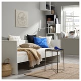 Modern minimalist bedroom with a white VIHALS daybed, blue and beige pillows, wooden shelves, and a wicker basket.
