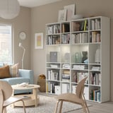 Large living room with light grey VIHALS bookshelf, filled with books and decor. Light blue sofa, wooden chairs, and colourful rug.