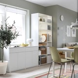 Modern dining room with white storage units, plant, lamp, table, and colourful rug.