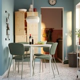 Modern dining room with white square VIHALS table, green round-backed chairs, turquoise wall, open doorway.