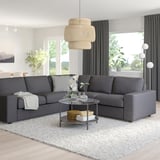 Modern living room with grey VIMLE sofa, glass coffee table, light rug, curtains, and pendant light.