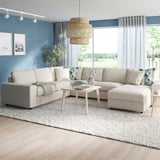 Bright living room with large l-shaped VIMLE beige sofa, wooden coffee table, and large windows. Modern light fixture, blue walls, and natural light.