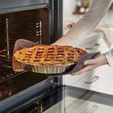 Person removing lattice pie from black oven.