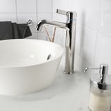 A VOXNAN chrome tap beside a white basin, with lever handle and ceramic discs, on a white tiled wall.
