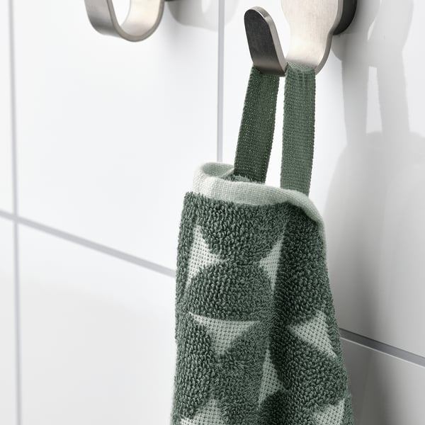A green and white textured towel hangs on a metallic hook, showcasing its absorbent terry side and patterned jacquard weave.