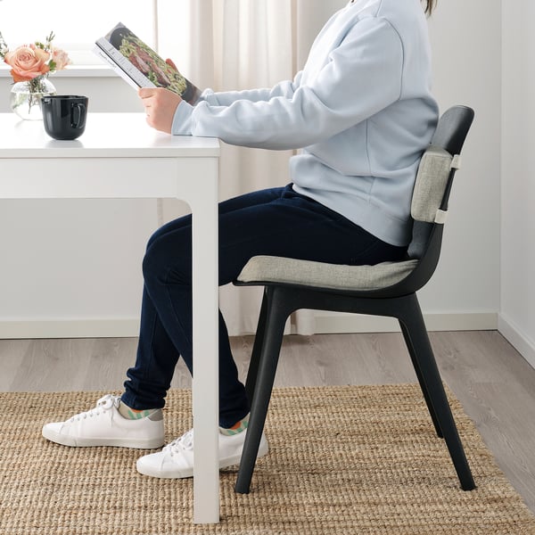 Person sitting on ÅKERVINDEFLY lumbar cushion while reading a book at a desk.