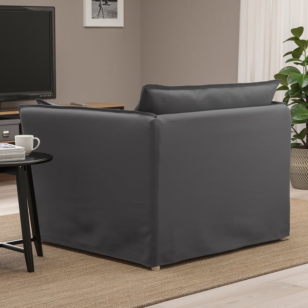 A grey armchair with high back and armrests in a living room. A side table with a mug sits beside it, near a tv.
