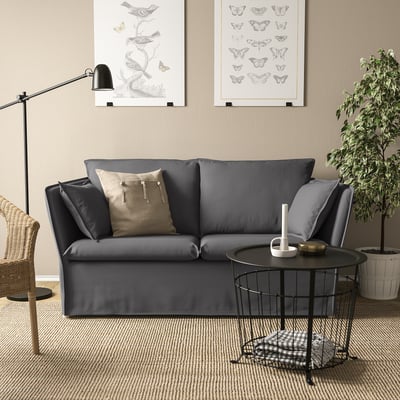 Modern living space with grey BACKSÄLEN sofa, black side table, floor lamp, wall art, and plant.