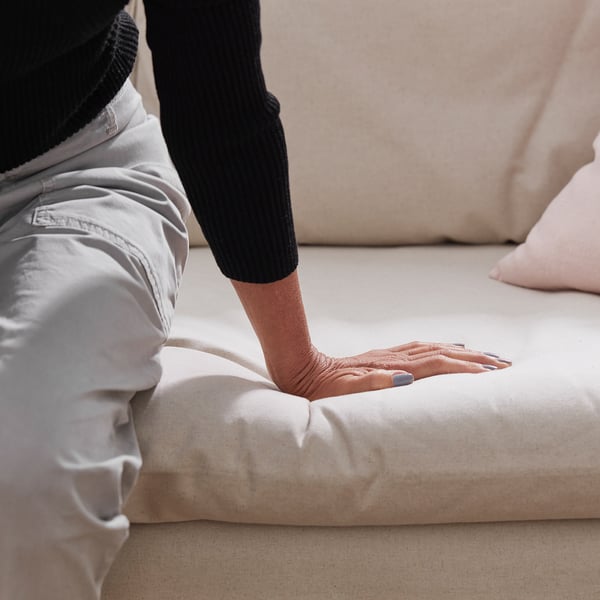 Person is testing softness of a white foam block. The block is part of a comfortable, easy-to-clean sofa with a removable machine-washable cover.