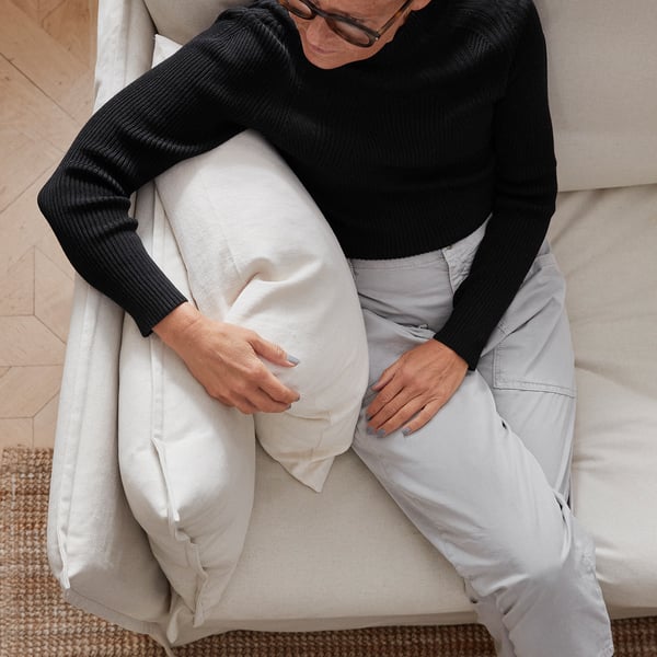 Person sitting on a comfortable, deep-seat sofa with a high back, likely from the BACKSÄLEN series, designed for relaxation.