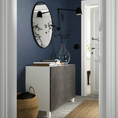 Grey BESTÅ sideboard with books, vase, and mirror in dark blue hall. Black basket and sconce.