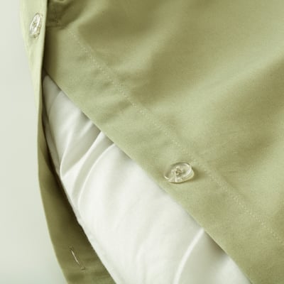 Close-up of light green duvet cover with button closure, showing sateen weave texture.
