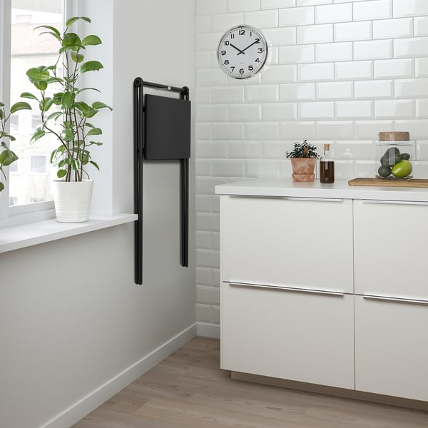 Modern kitchen with foldable wall-mounted table, plants, and white clock.