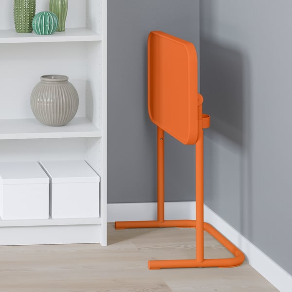 Bright orange laptop stand in corner, adjustable, near shelves.