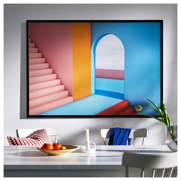 Large colourful staircase art print, pink steps, blue wall. Framed in black, hangs above table with chairs & decor.