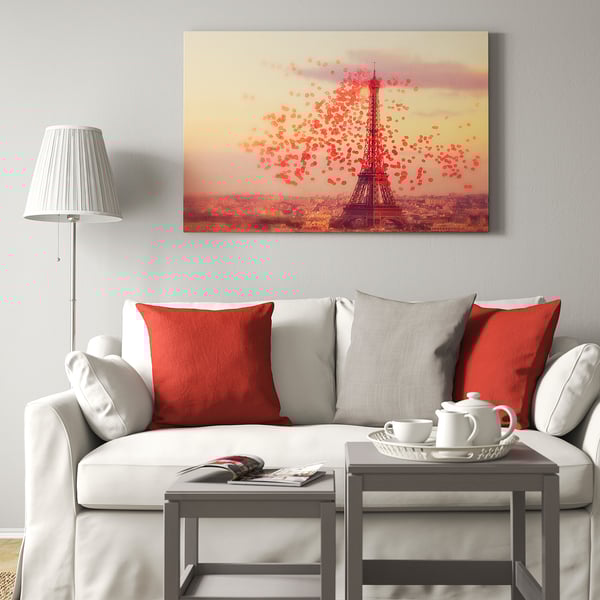 Modern living room with large eiffel tower artwork, red pillows on grey couch, white tea set on table, lamp to left.