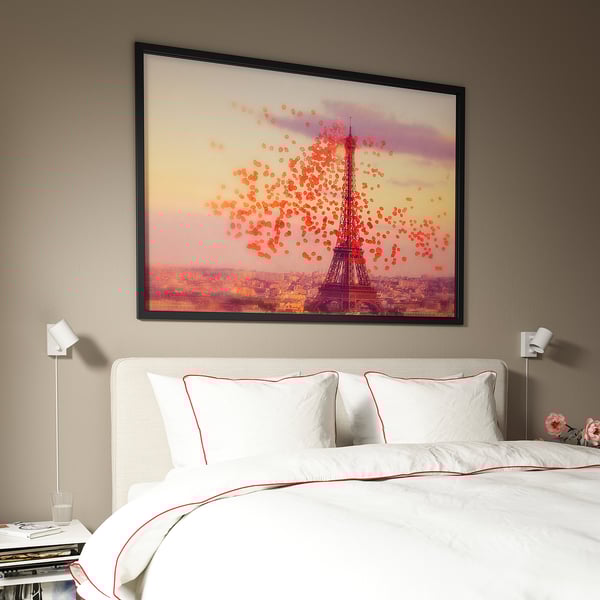 BJÖRKSTA framed eiffel tower art above bed in stylish bedroom with red accents and wall lights.