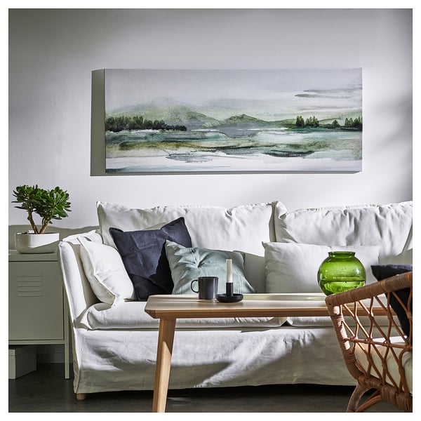 Modern living room with white couch, green pillows, wooden table, plant, and large rectangular framed art on white wall.