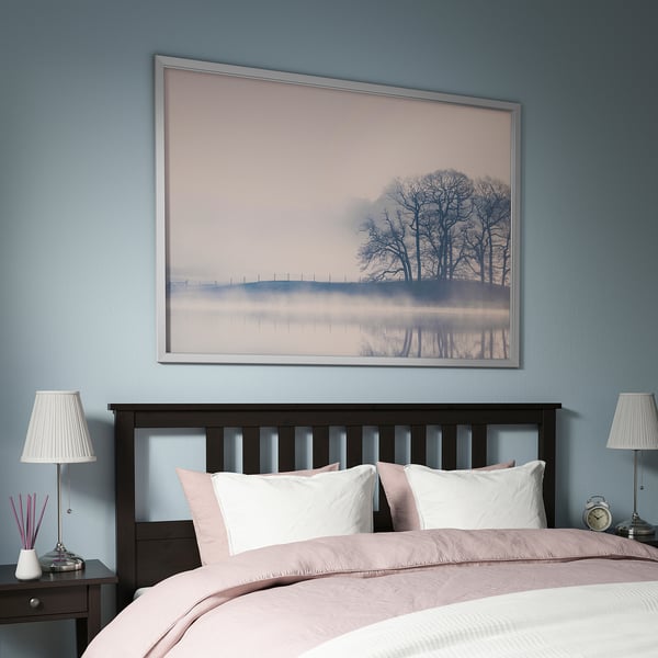 Blue bedroom with BJÖRKSTA picture, white bed, pink accents, dark nightstands, lamps, clock.
