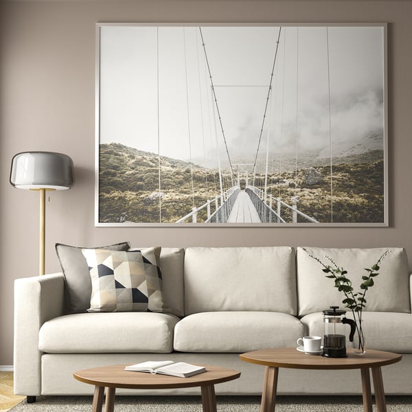 Bridge photo over couch in living room. Couch with pillows, tables with plant and coffee press, lamp nearby.