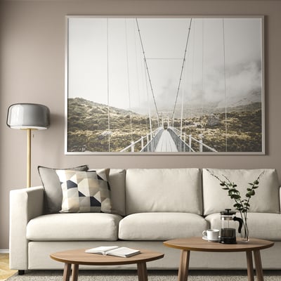 Bridge photo over couch in living room. Couch with pillows, tables with plant and coffee press, lamp nearby.