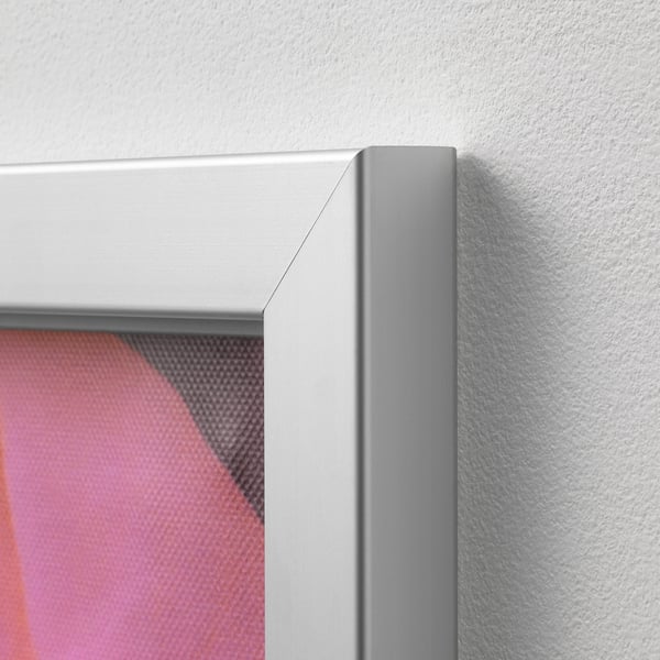 A close-up of a sleek, silver-framed canvas art, mounted on a plain wall. The corner of the frame is neatly angled, showcasing quality craftsmanship.