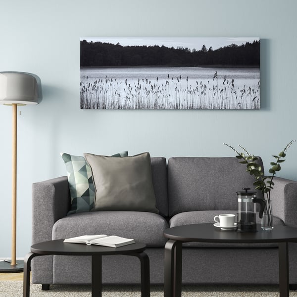 Minimalist living room with grey bjorksta artwork above sofa, calm lake scene, coffee maker, greenery, grey lamp.
