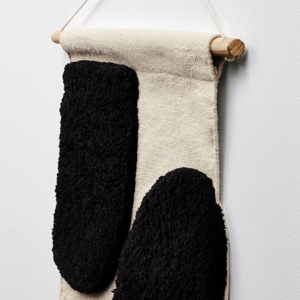 A handcrafted wall hanging with black and white textured fabric, featuring a natural bamboo hanger.
